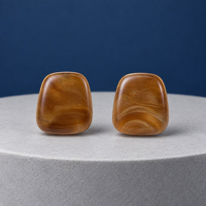 Chestnut Cabochon Studs marbled brown cushion stud earrings on a cream stone pedestal