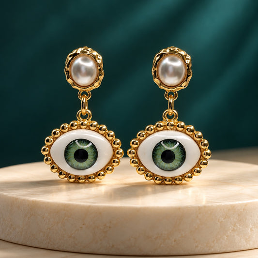 Gilded Evil Eye Pearl Drops gold-tone evil eye pearl drop earrings styled on cream marble