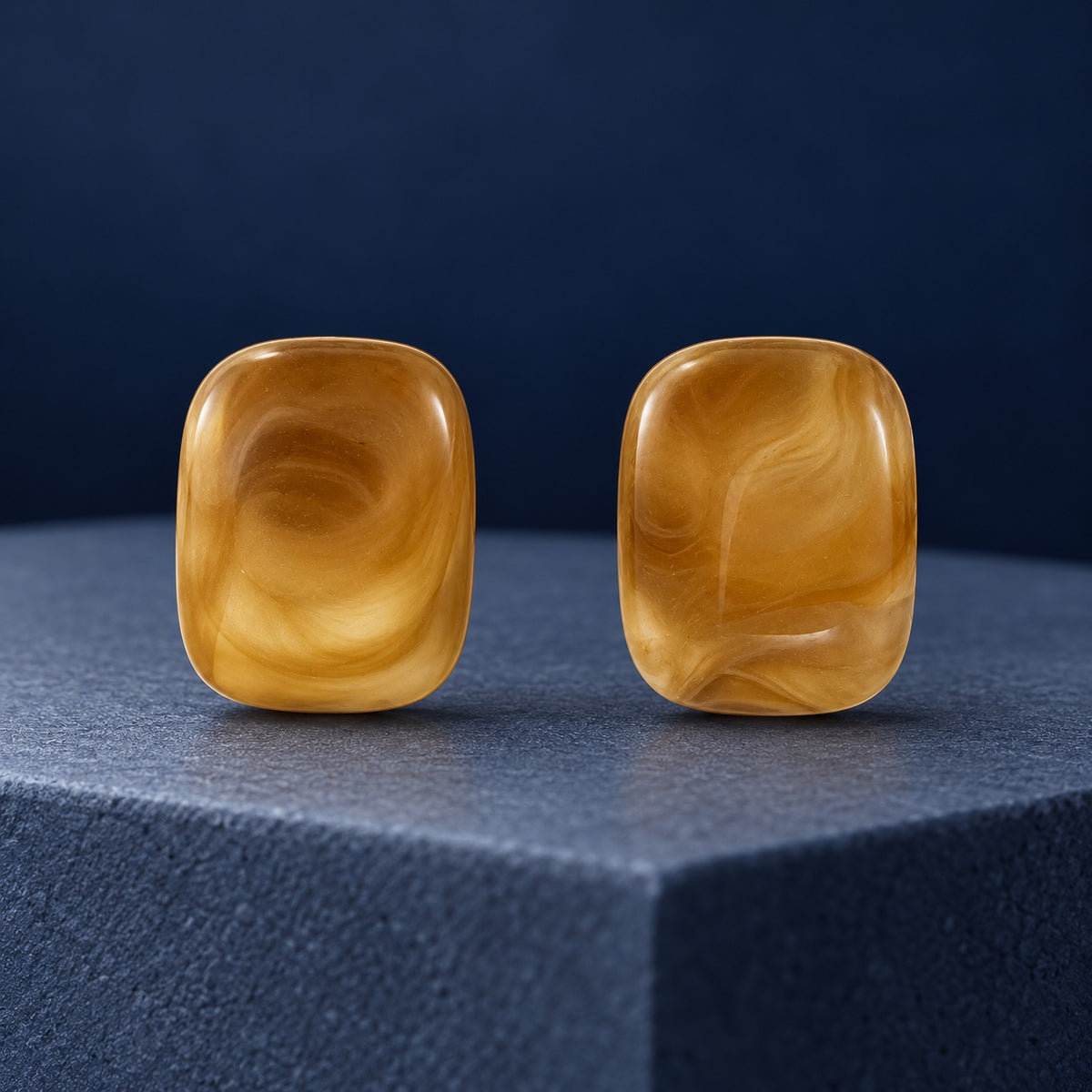 Golden Honey Swirl Cabochon Studs with glossy caramel marbled cushion stones on a travertine ledge