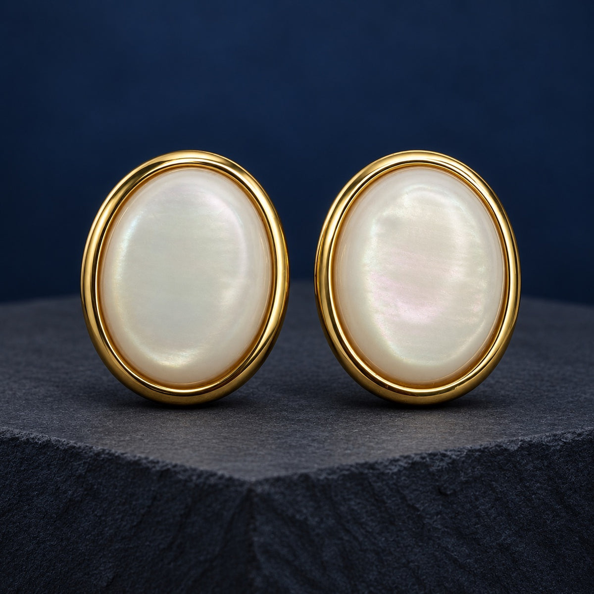 Pearlescent Oval Dome Stud Earrings in gold tone with a milky white stone on a marble ledge