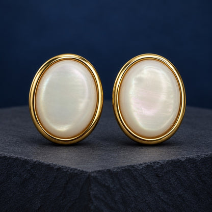 Pearlescent Oval Dome Stud Earrings in gold tone with a milky white stone on a marble ledge