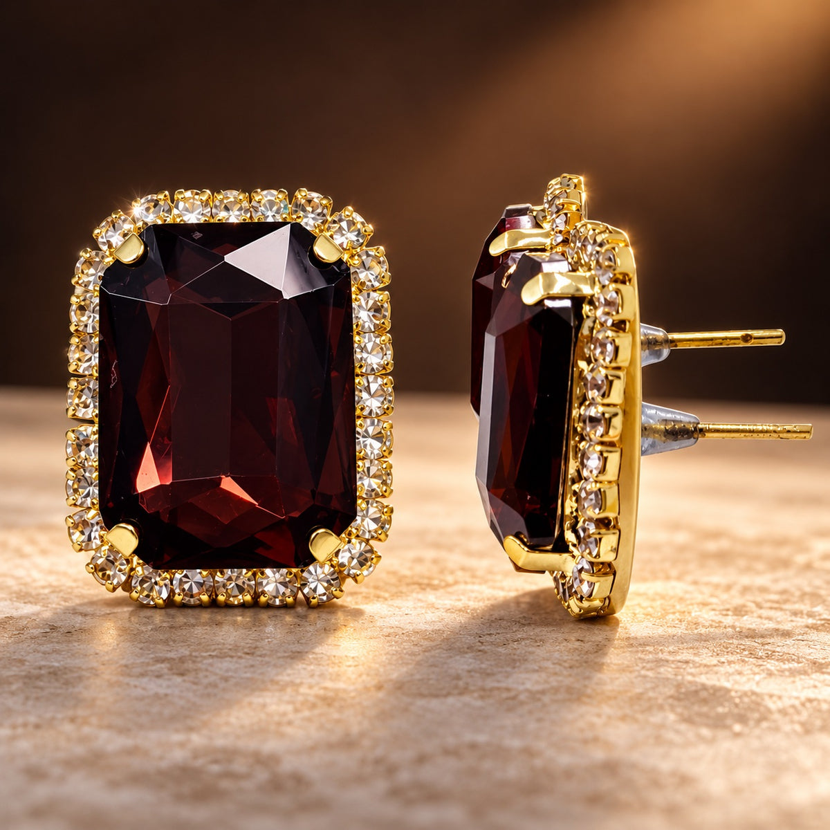 Regal Wine Halo Studs gold-tone earrings with a faceted deep wine centre stone and sparkling halo on a styled surface