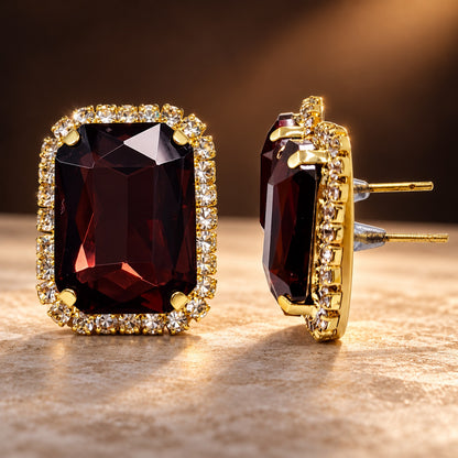 Regal Wine Halo Studs gold-tone earrings with a faceted deep wine centre stone and sparkling halo on a styled surface